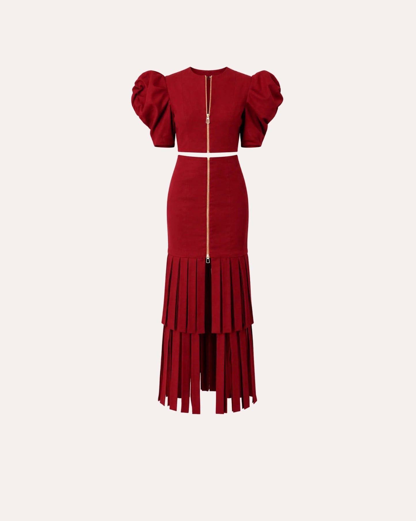 A red two-piece dress set featuring a short puff-sleeve crop top and a matching high-waisted pleated skirt with a central gold zipper, shown against a plain white background.